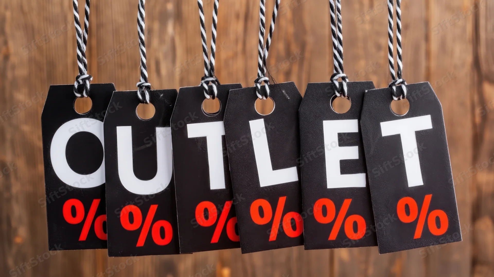Black sale tags spelling outlet with red percent symbols hanging on striped strings against wooden background