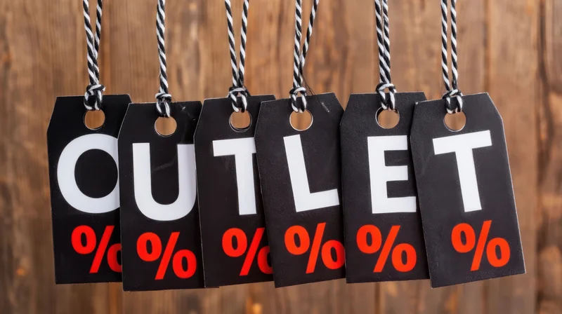 Black sale tags spelling outlet with red percent symbols hanging on striped strings against wooden background