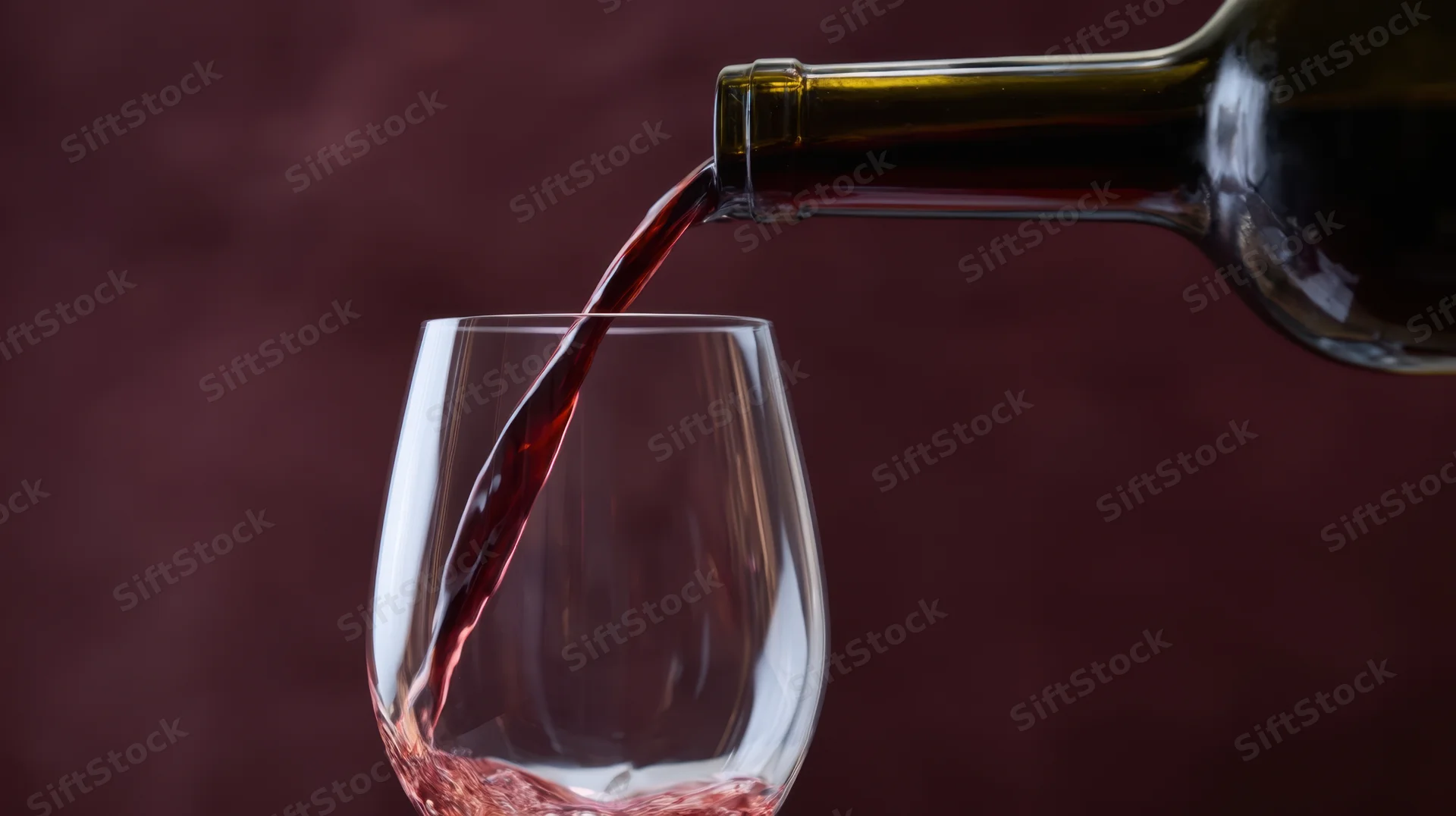 Red wine being poured from a bottle into a glass against a dark maroon background