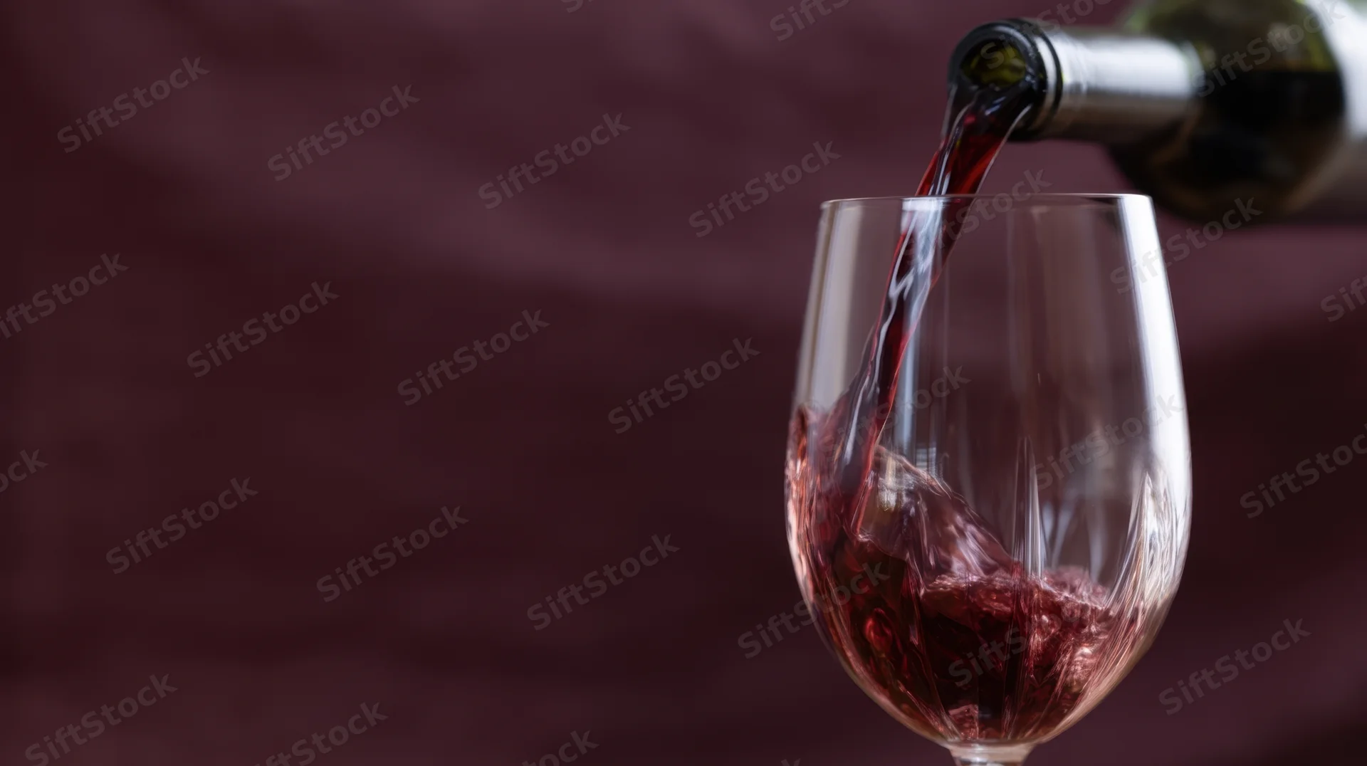 Red wine being poured from a bottle into a glass against a dark maroon background