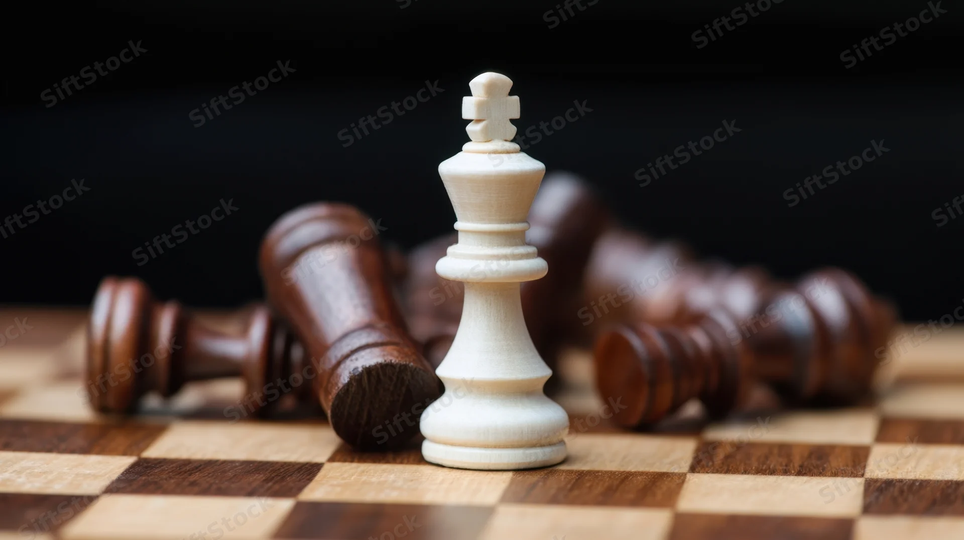 White chess king standing upright on a wooden board with fallen dark pieces around it