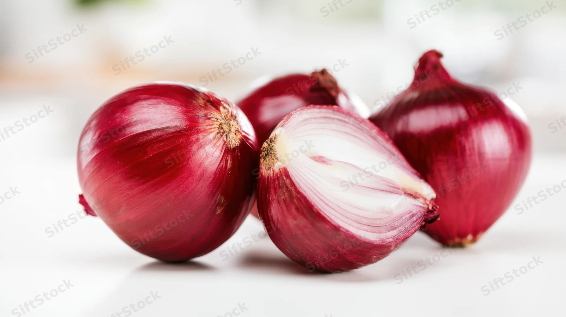 Four red onions arranged on a white surface with one cut in half showing layers