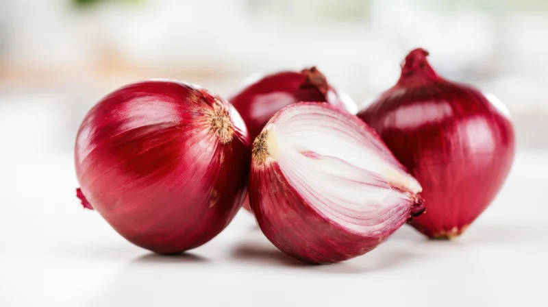 Four red onions arranged on a white surface with one cut in half showing layers
