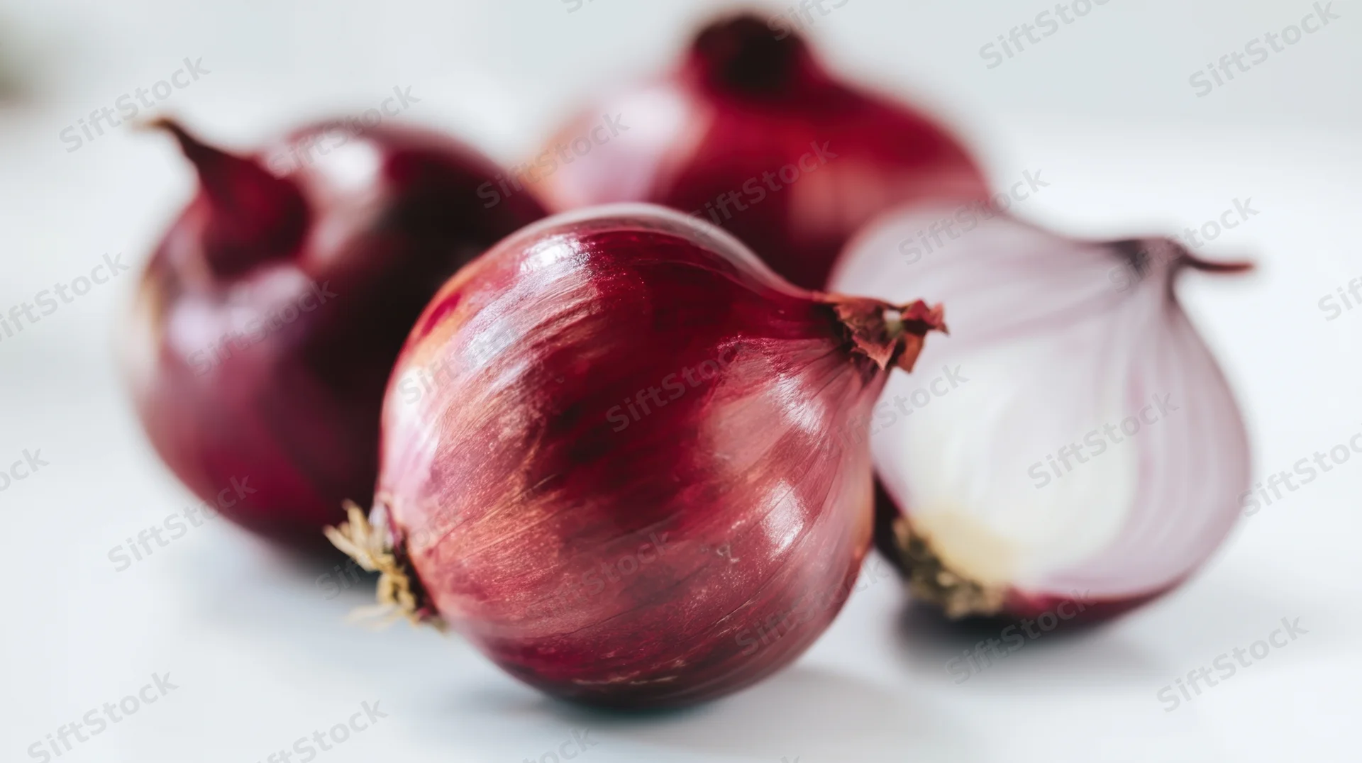Four red onions arranged on a white surface with one partially peeled, close-up view