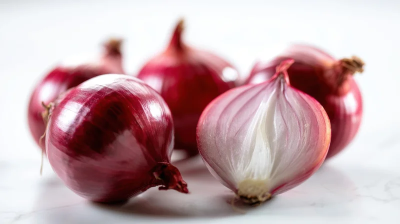 Red onions arranged on a white marble surface, one partially peeled to show inner layers