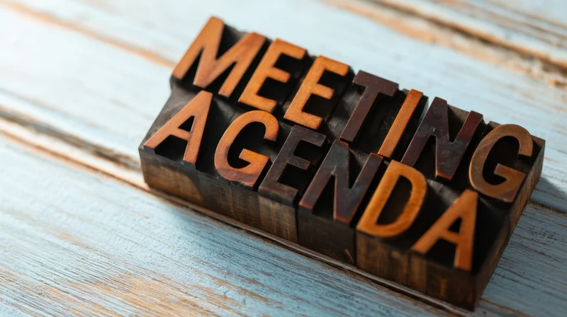Wooden letterpress blocks spelling meeting agenda on a blue painted wooden surface