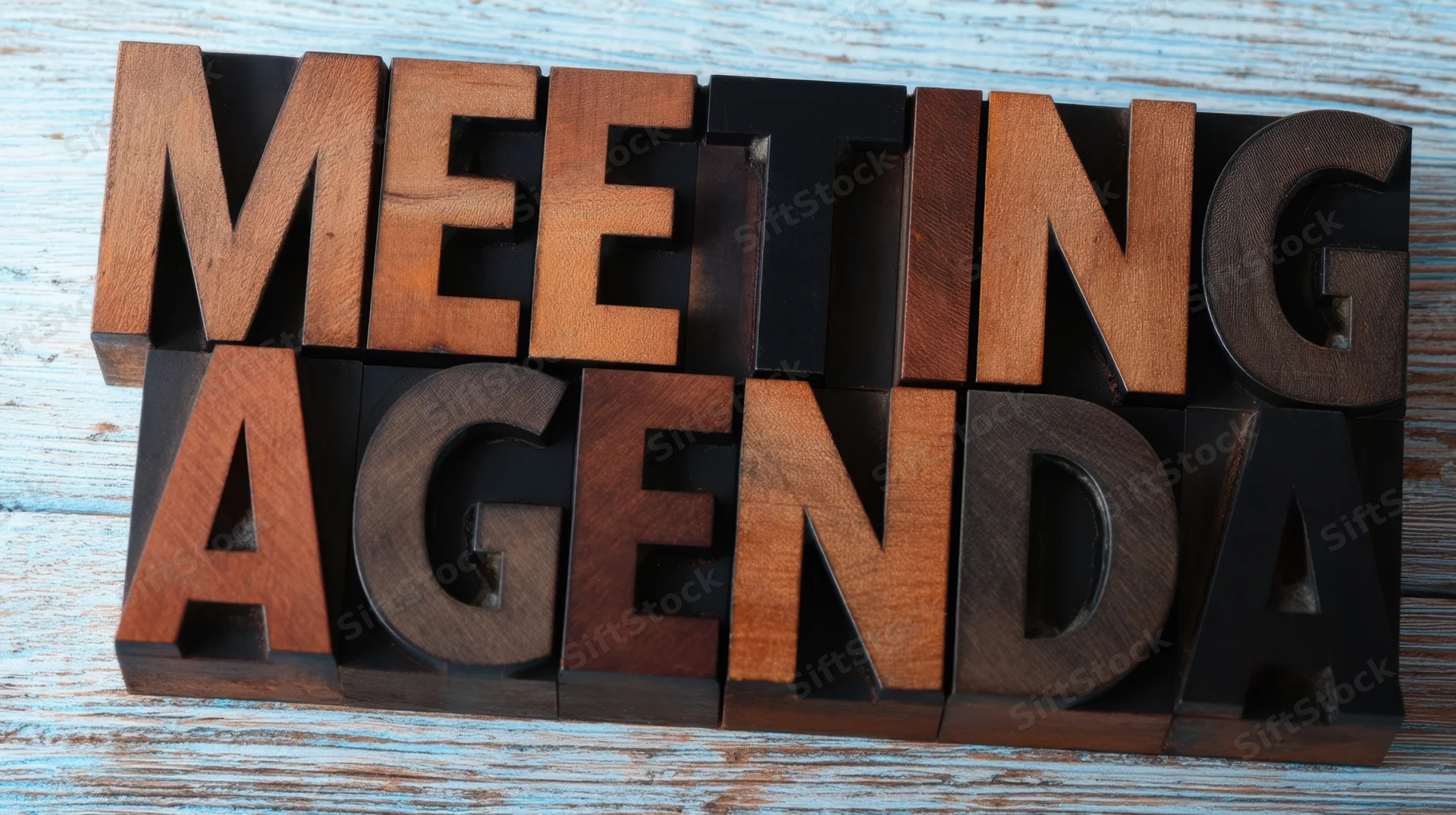 Wooden block letters spelling meeting agenda on a weathered blue wooden surface