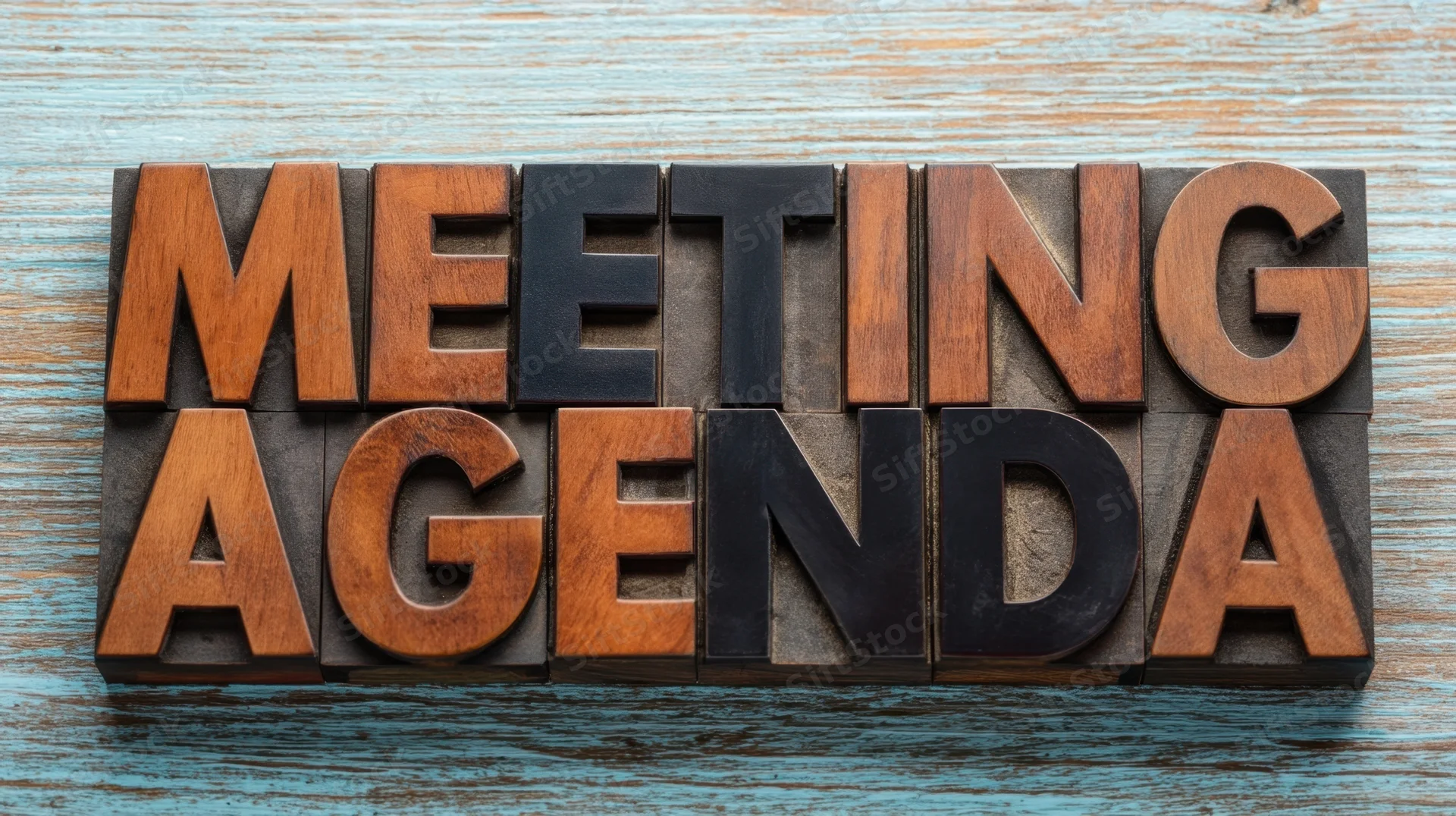 Wooden letterpress blocks spelling meeting agenda on a blue textured surface