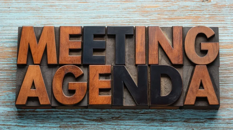 Wooden letterpress blocks spelling meeting agenda on a blue textured surface