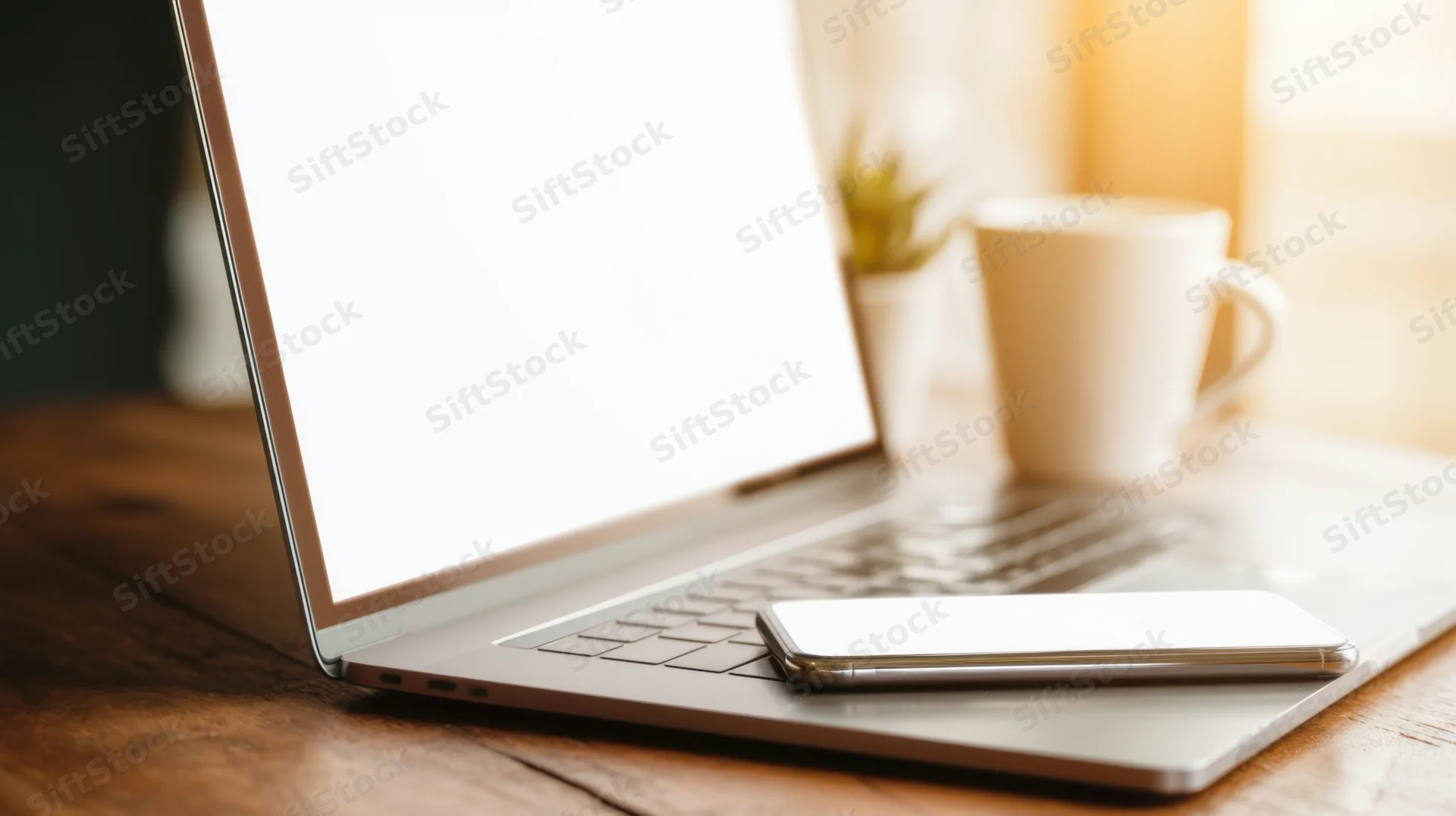 Laptop with blank screen and smartphone on wooden desk in home office setting
