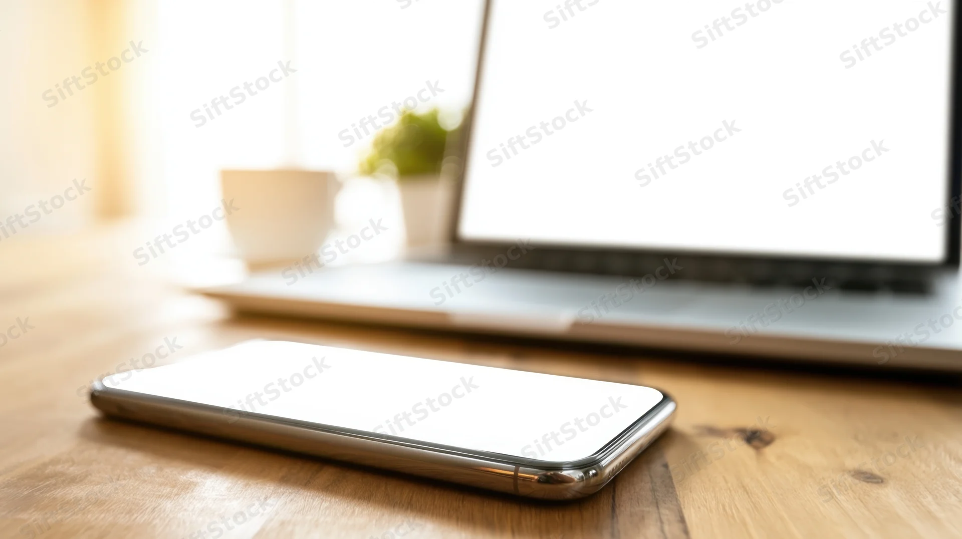 Smartphone with blank screen on wooden desk beside laptop in home office setting