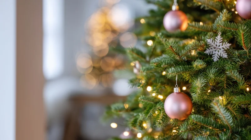Closeup of decorated christmas tree with pink baubles and silver snowflake ornaments, warm lights glowing in soft focus background