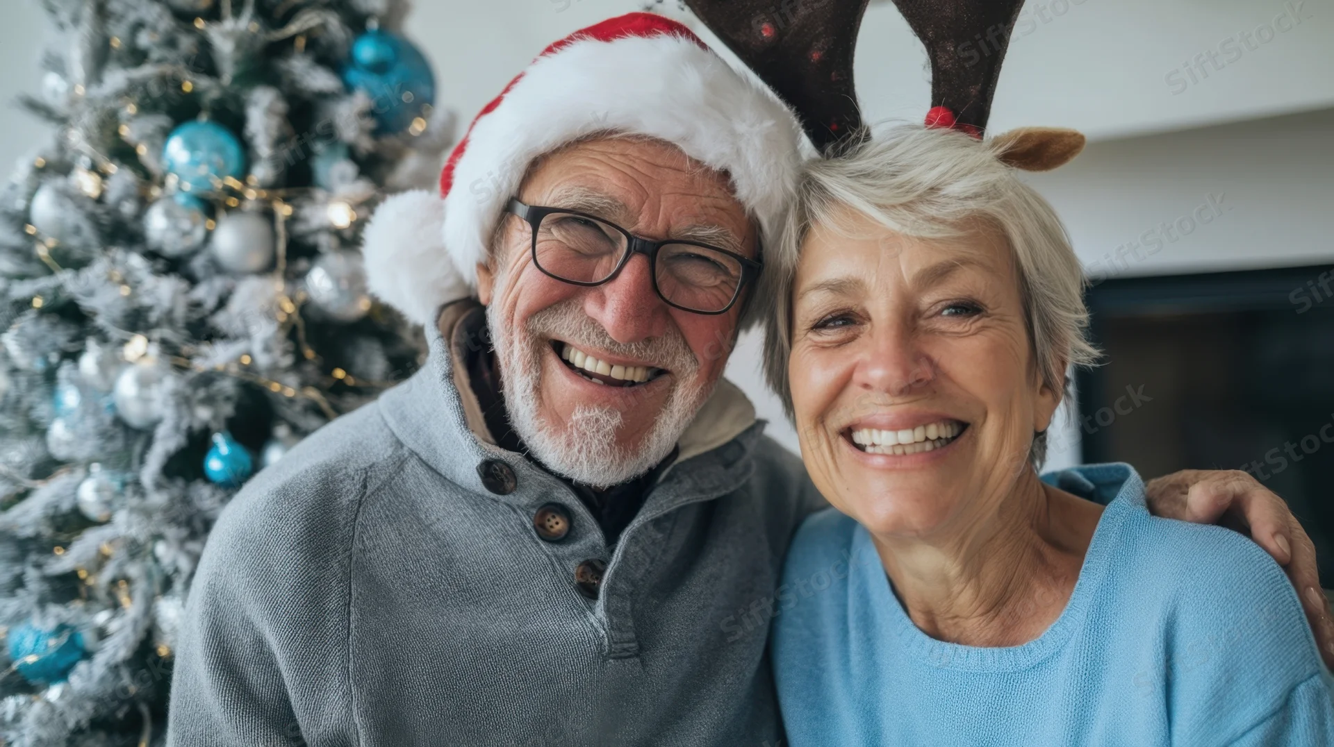 Cheerful senior couple smiling together in front of a decorated christmas tree wearing festive hats