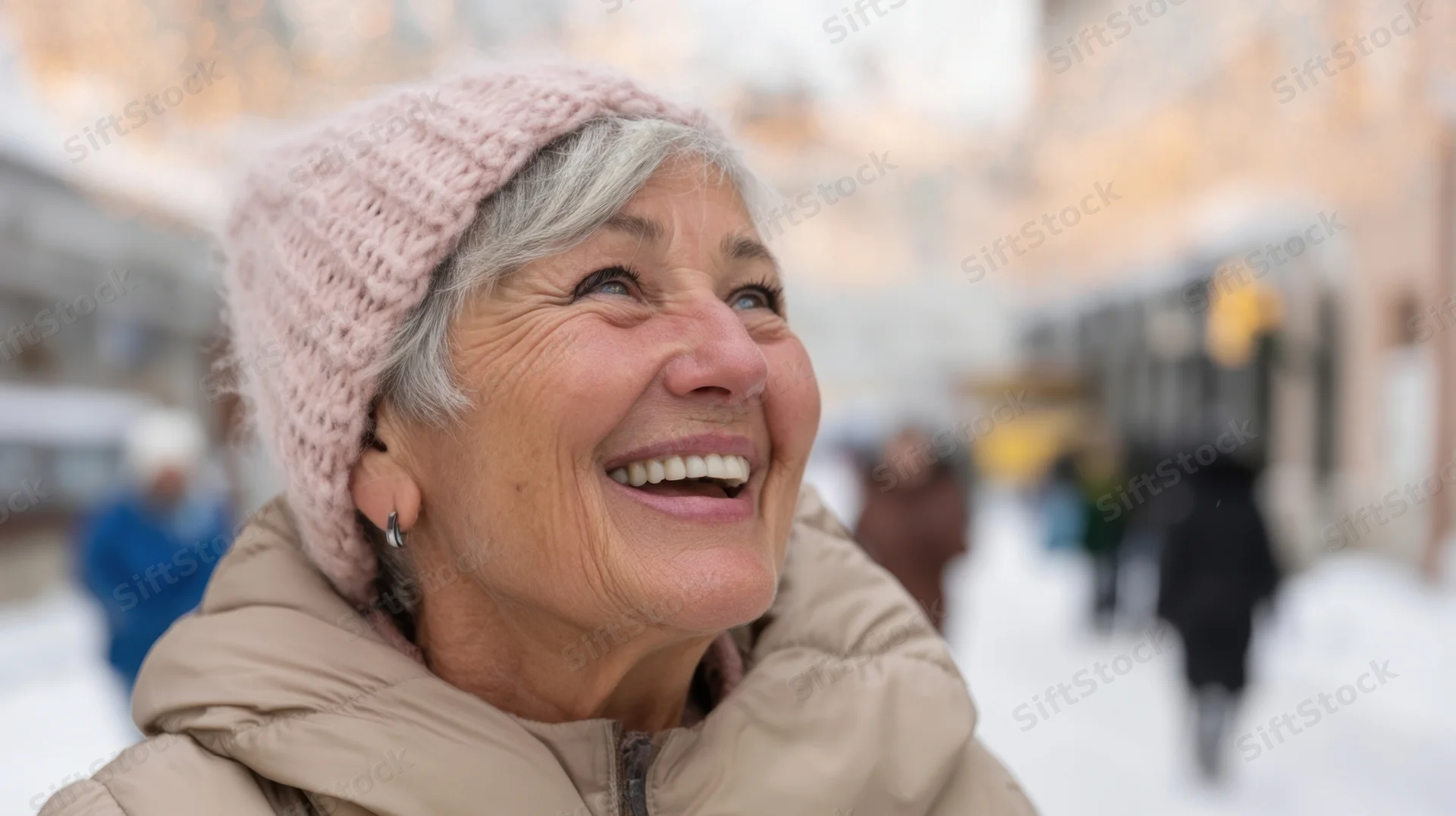 Senior woman smiling outdoors in snowy city street wearing pink knitted hat and beige puffer coat