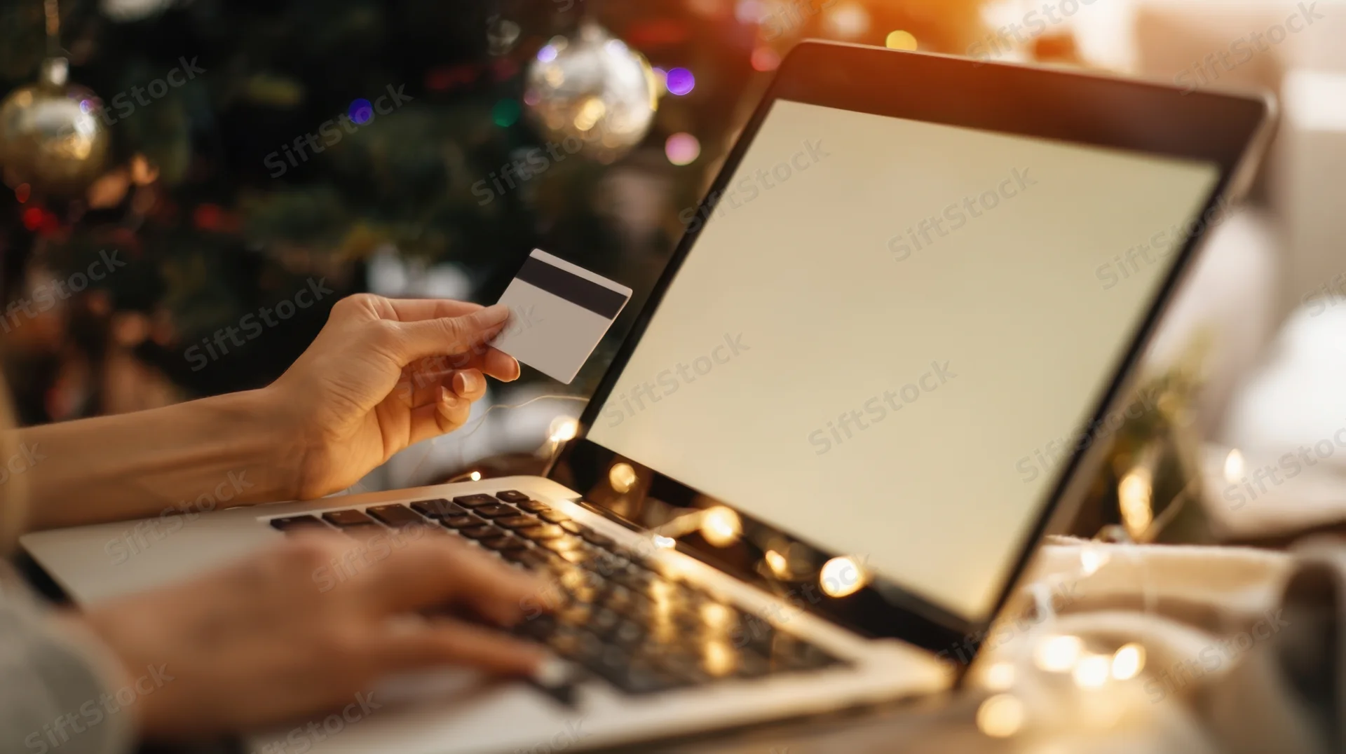 Woman's hands typing on laptop while holding credit card in front of decorated christmas tree