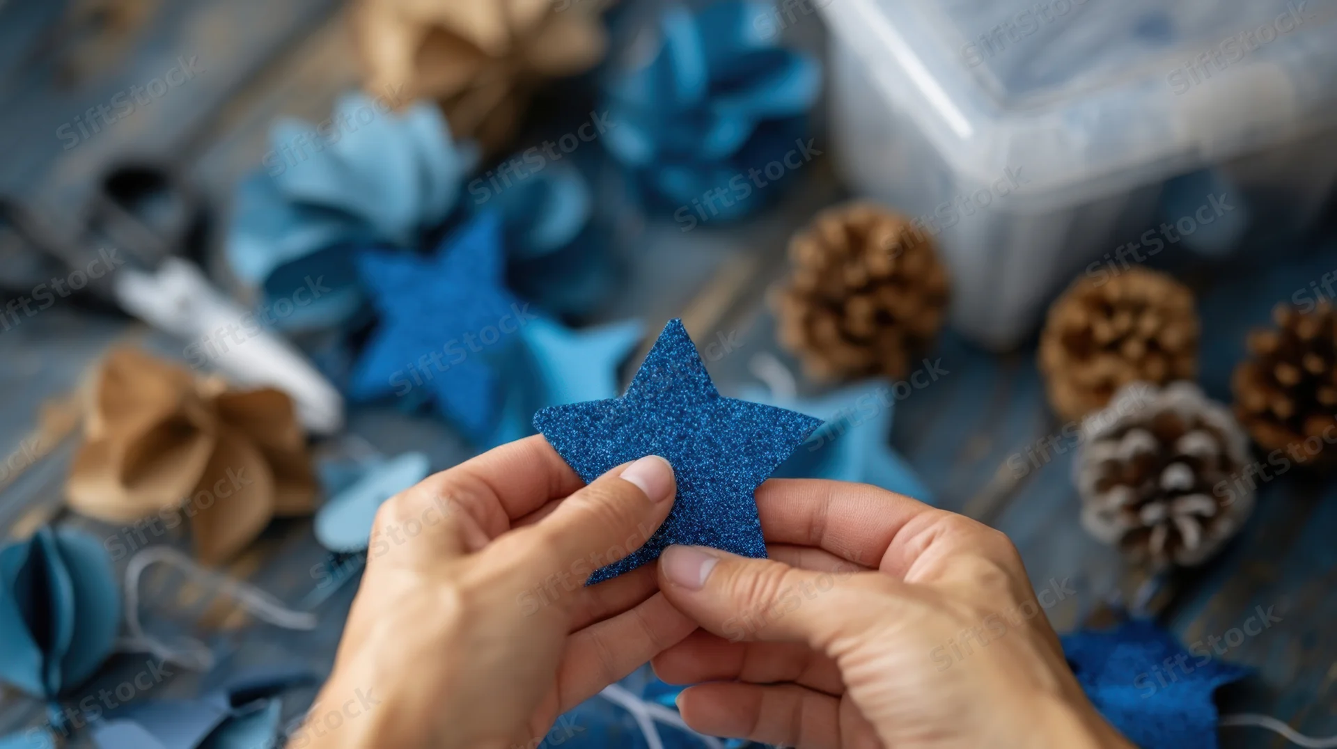 Hands holding a blue glitter star decoration among crafting supplies on a wooden table