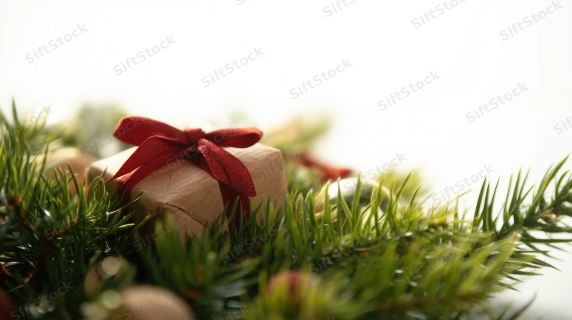 Gift box wrapped in brown paper with red ribbon nestled among pine branches in a holiday wreath