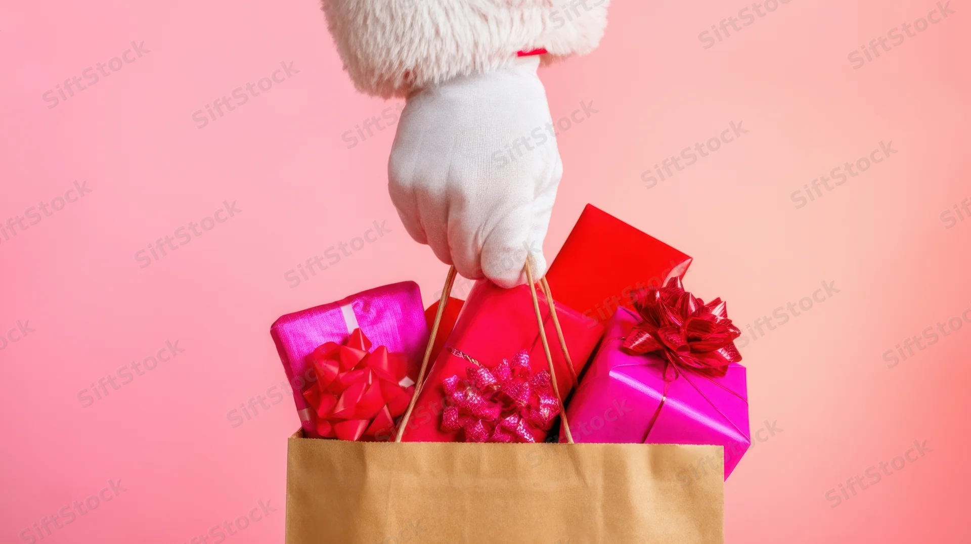 Santa's gloved hand holding a bag filled with wrapped gifts against a pink background