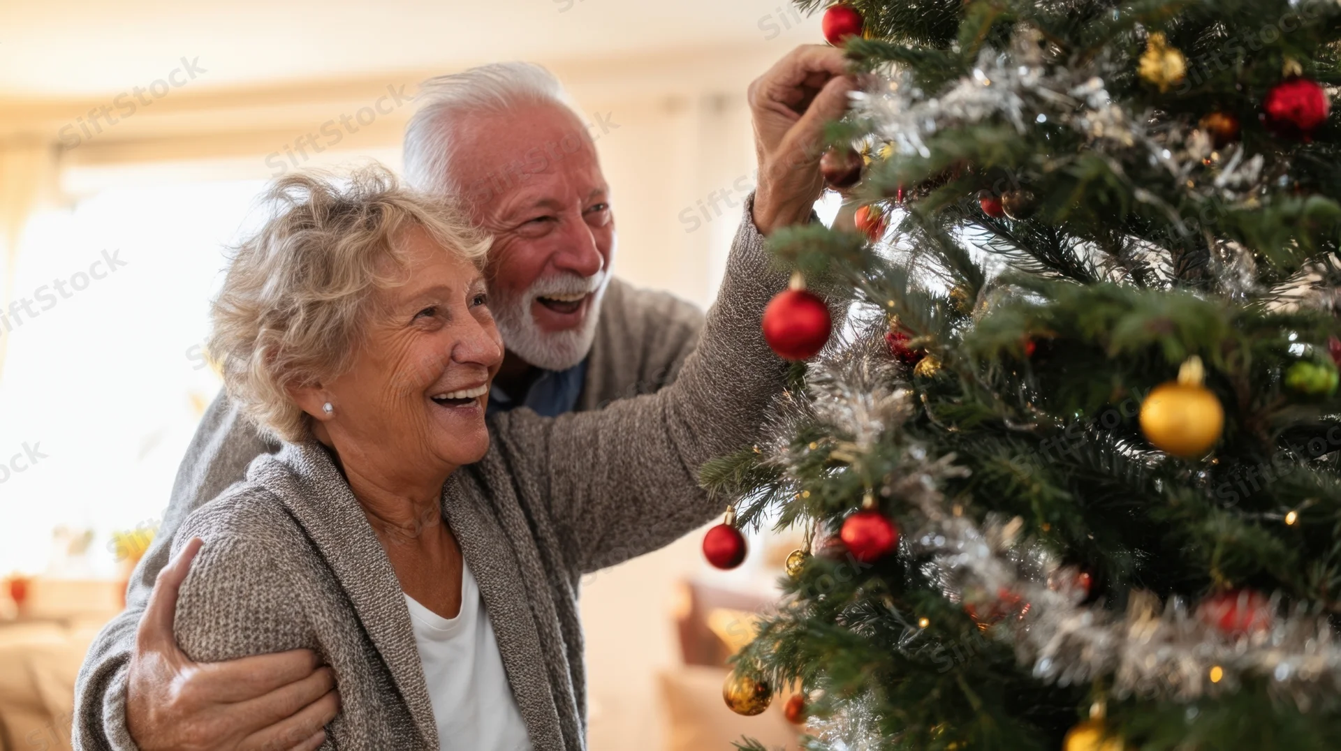 Elderly couple smiling and decorating a christmas tree together in their living room