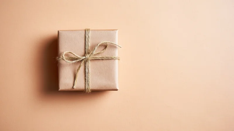 A gift box wrapped in kraft paper with twine bow on a beige surface