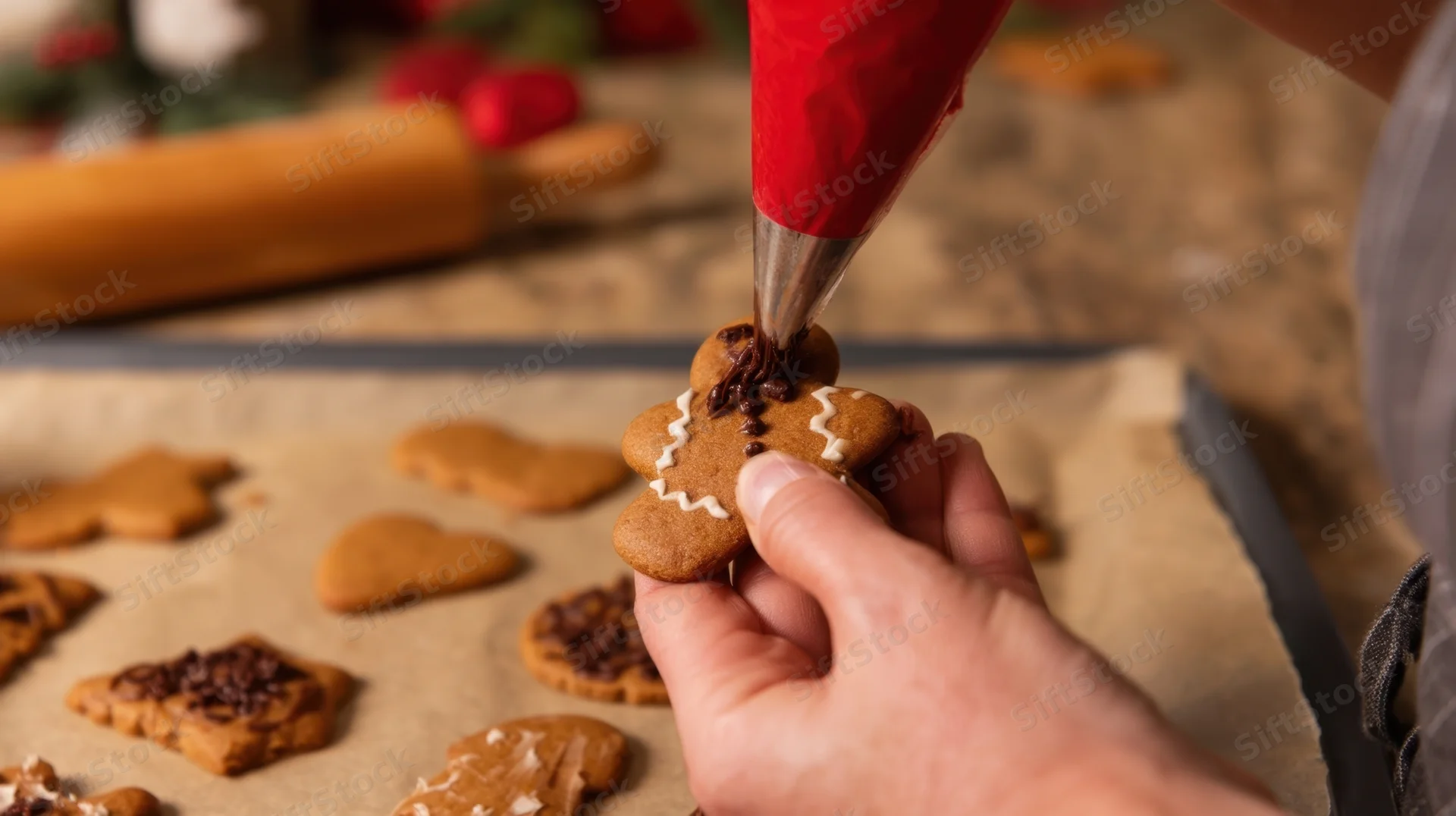 Person decorating gingerbread cookie with icing on parchment-lined tray in kitchen