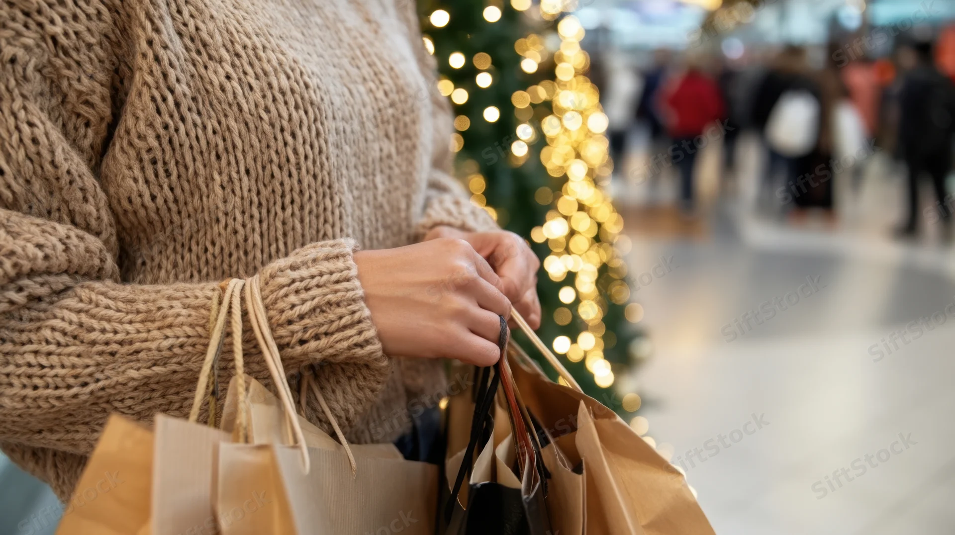 Woman holding multiple shopping bags in a mall with a decorated christmas tree in the background