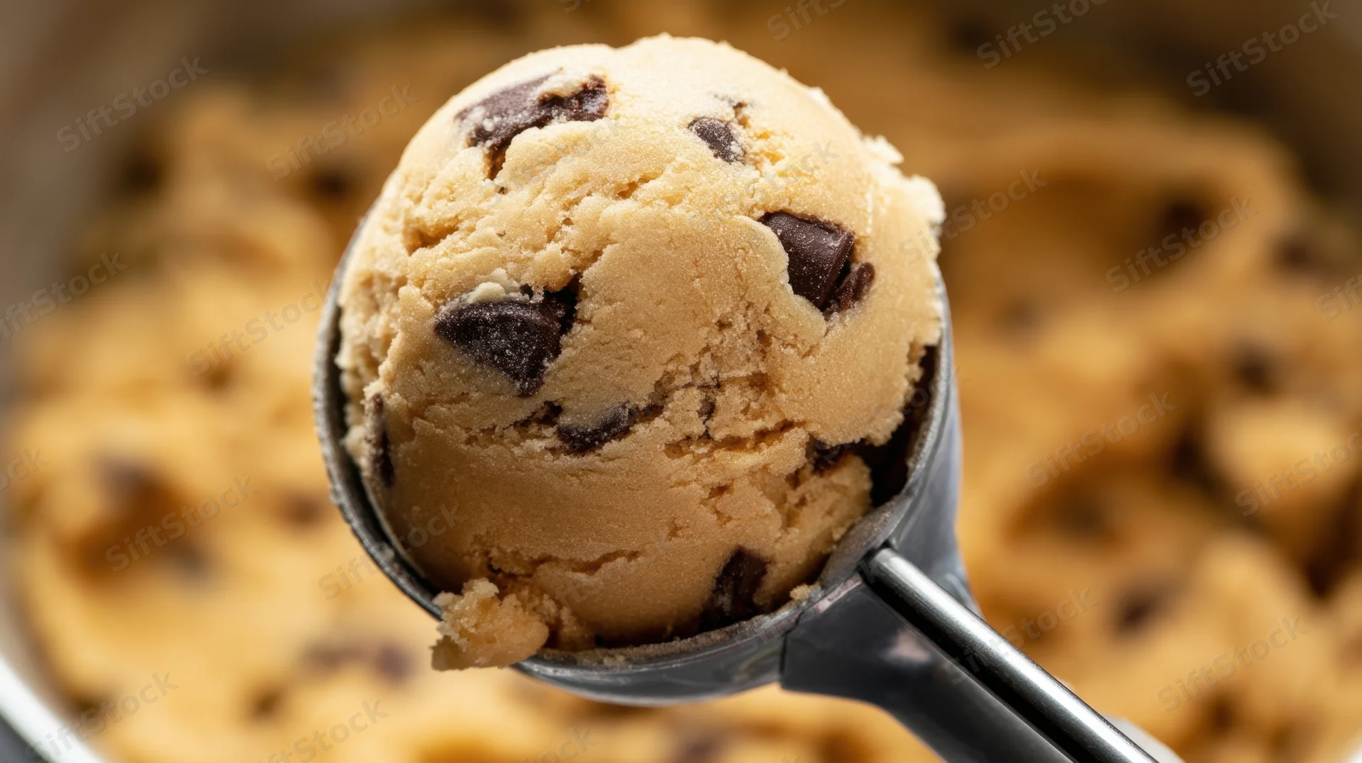 Metal scoop holding a ball of chocolate chip cookie dough above a mixing bowl