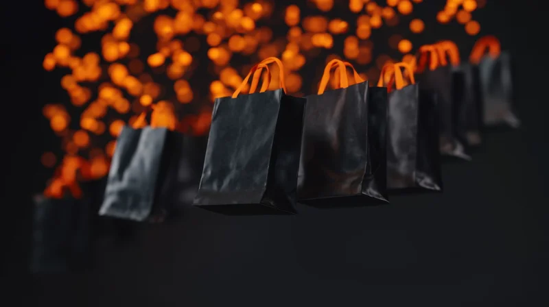 Black shopping bags with orange handles suspended in front of glowing bokeh lights