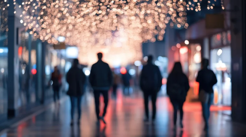 Silhouetted pedestrians walking along a festive shopping street at night under glowing holiday lights