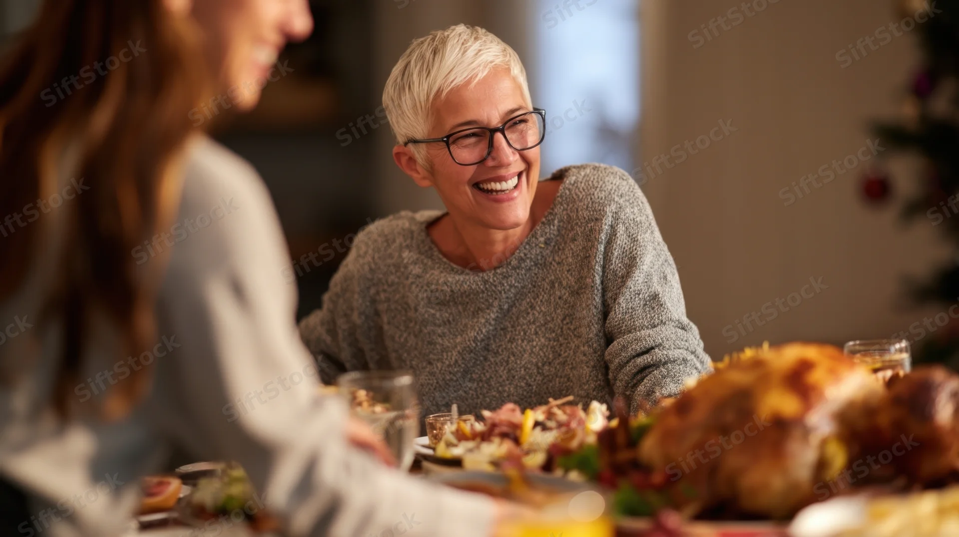 Senior woman laughing at a family dinner table with turkey and holiday decorations