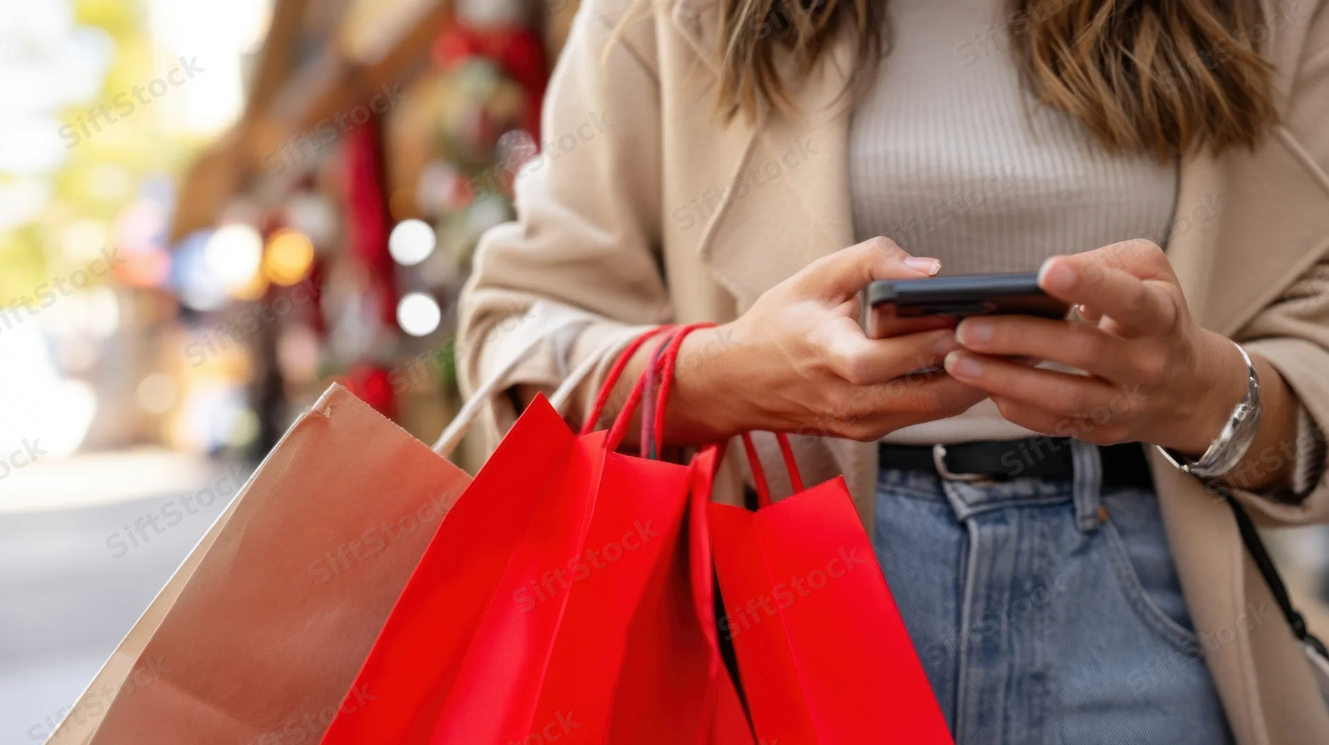 Woman using smartphone while holding shopping bags on city street