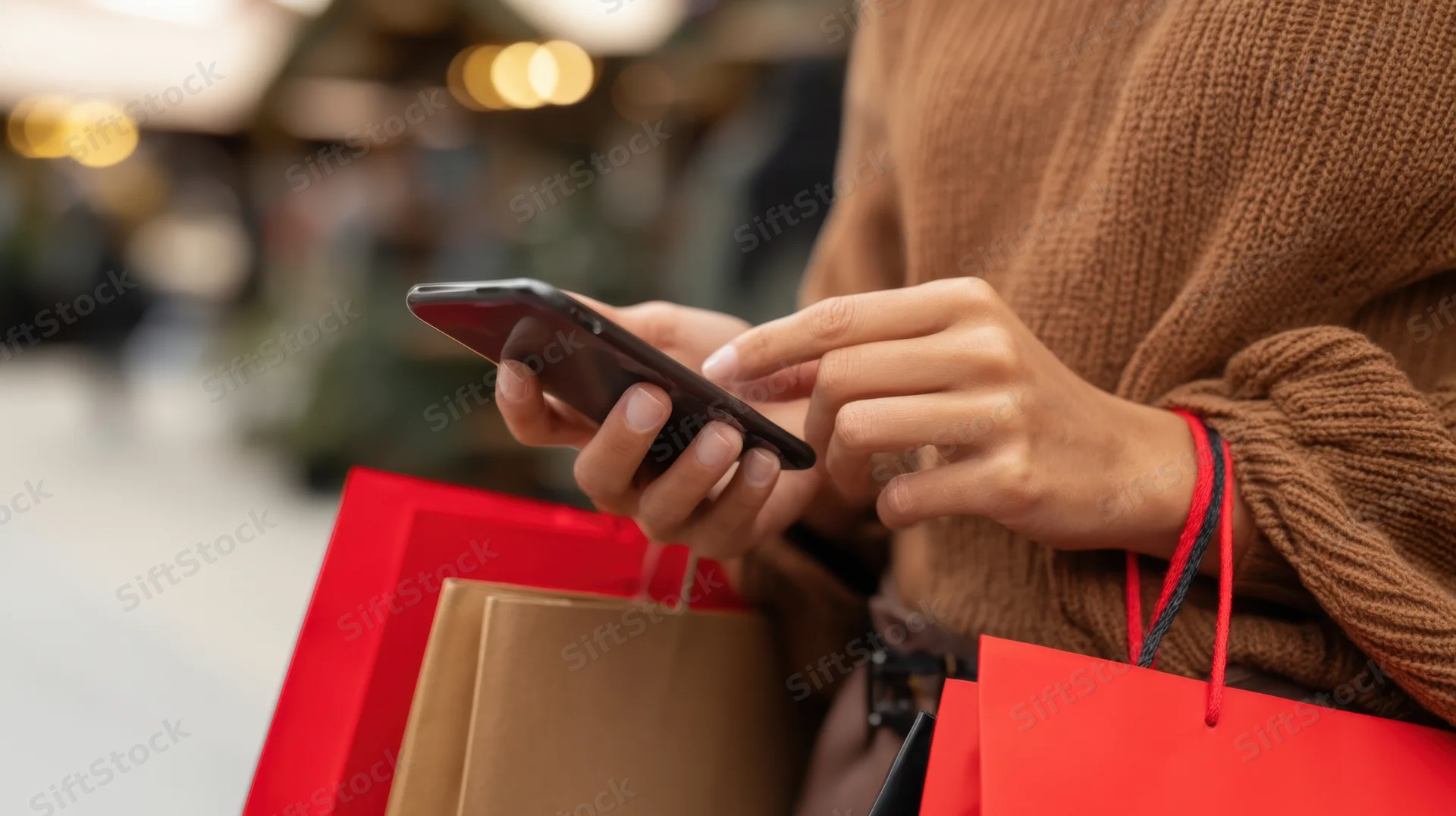 Woman using smartphone while holding shopping bags in urban setting