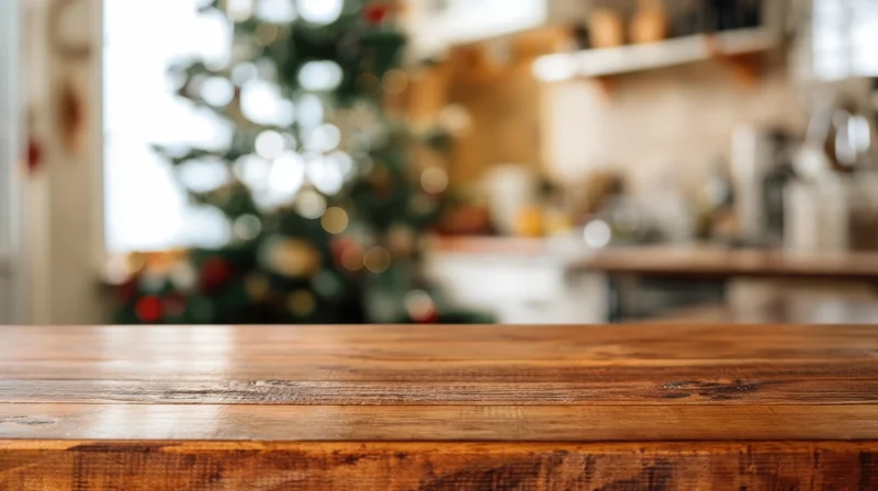 Wooden table in foreground with blurred christmas tree and kitchen decor in background