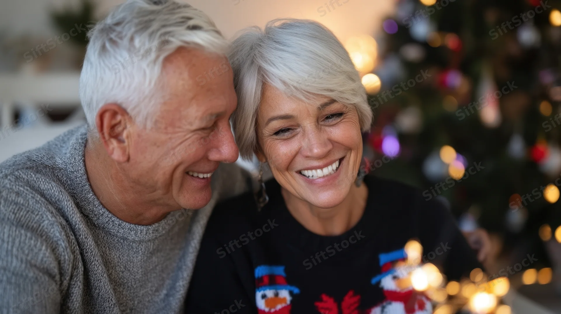 Senior couple smiling warmly at each other in front of a decorated christmas tree