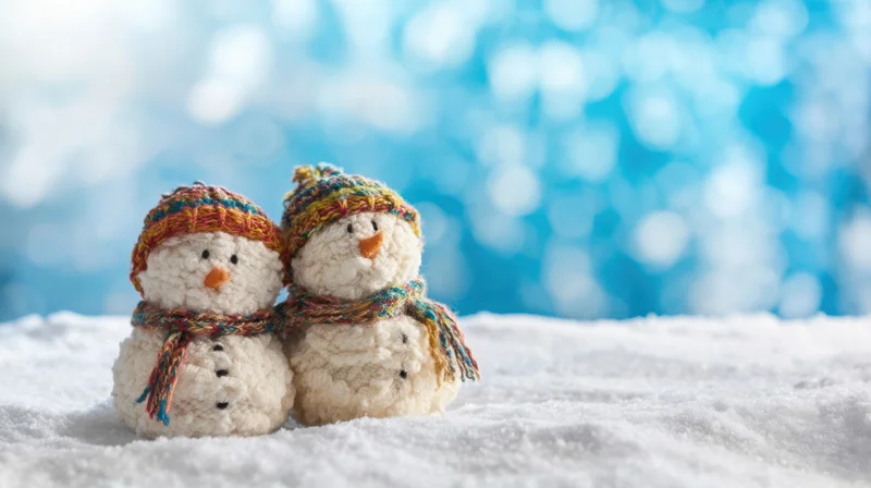 Two knitted snowmen wearing colorful hats and scarves sitting on snow with a blue bokeh background