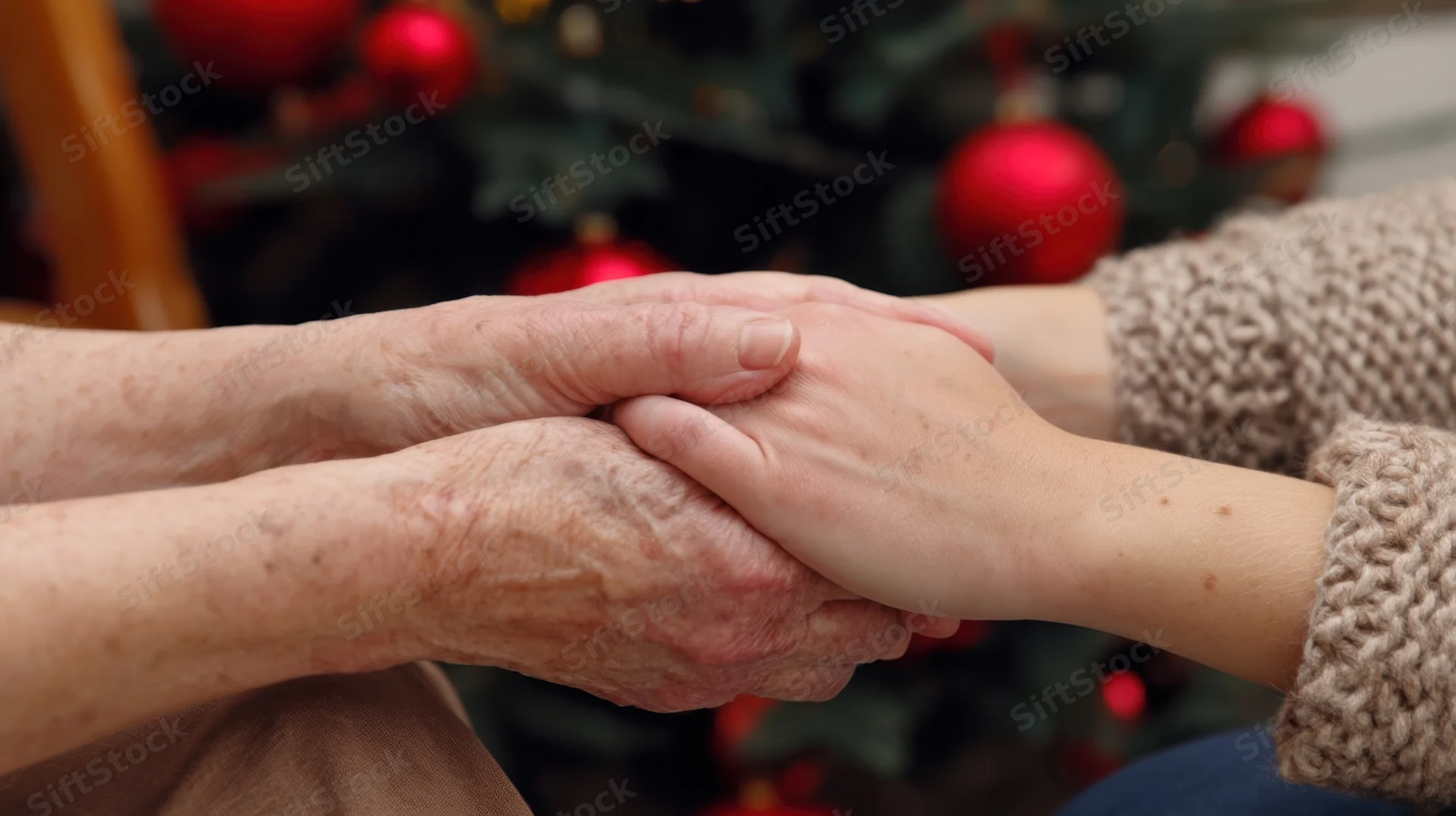 Elderly woman's hands gently held by a young person in front of a decorated christmas tree