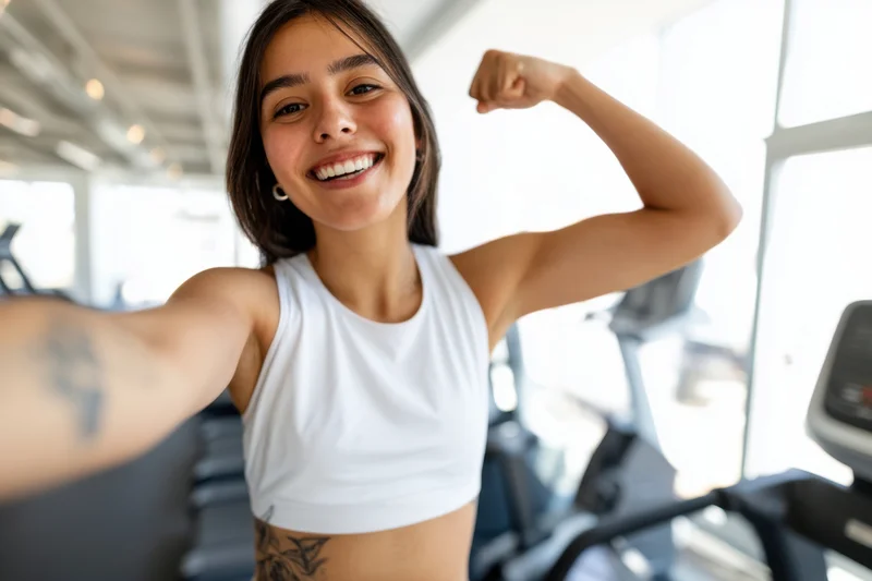 The Woman Celebrating Fitness With Selfie And Flexed Arm In Bright Gym