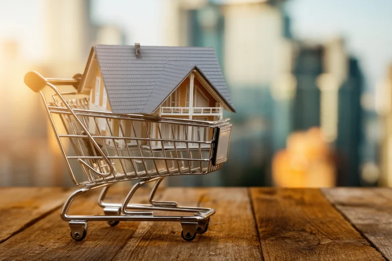 Miniature house in a shopping cart on a wooden table with city skyline in background