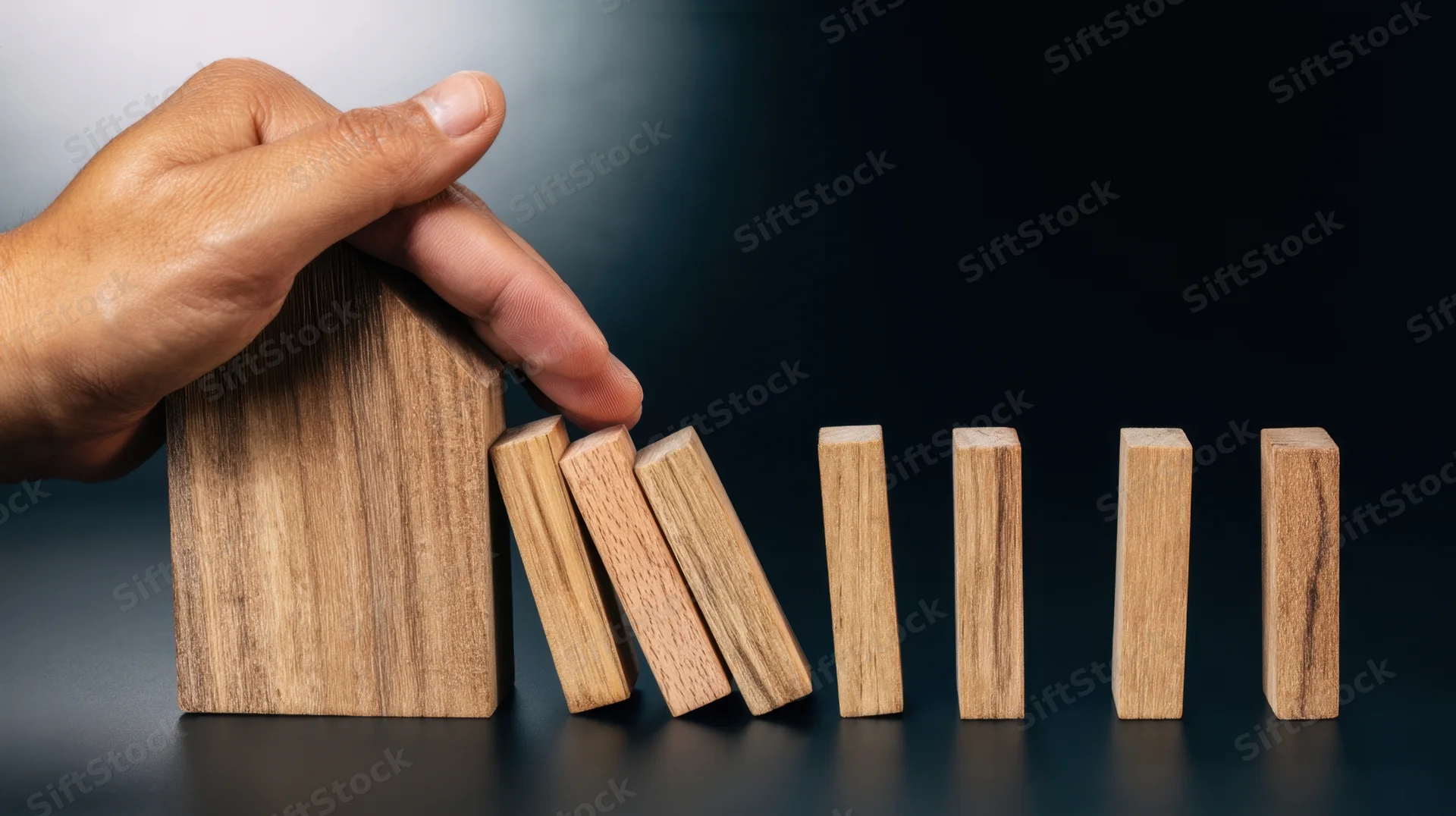 Hand holding wooden house block to stop falling dominoes in a row