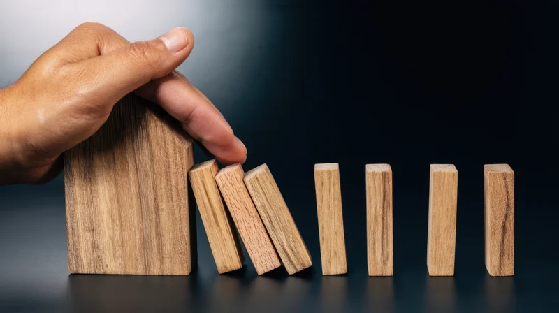 Hand holding wooden house block to stop falling dominoes in a row