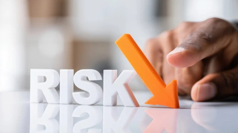 Hand pointing at orange arrow next to white 3d letters spelling risk on glossy surface