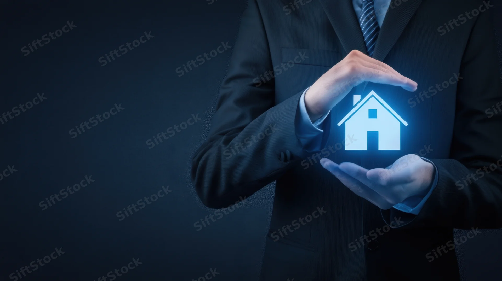 Businessman in suit holding glowing holographic house symbol with hands in protective gesture against dark background