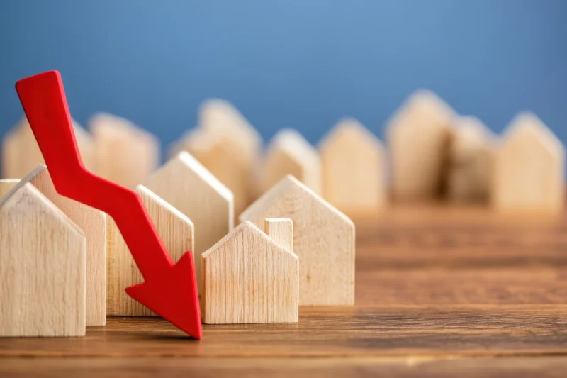 Red arrow pointing down over wooden house models on a table