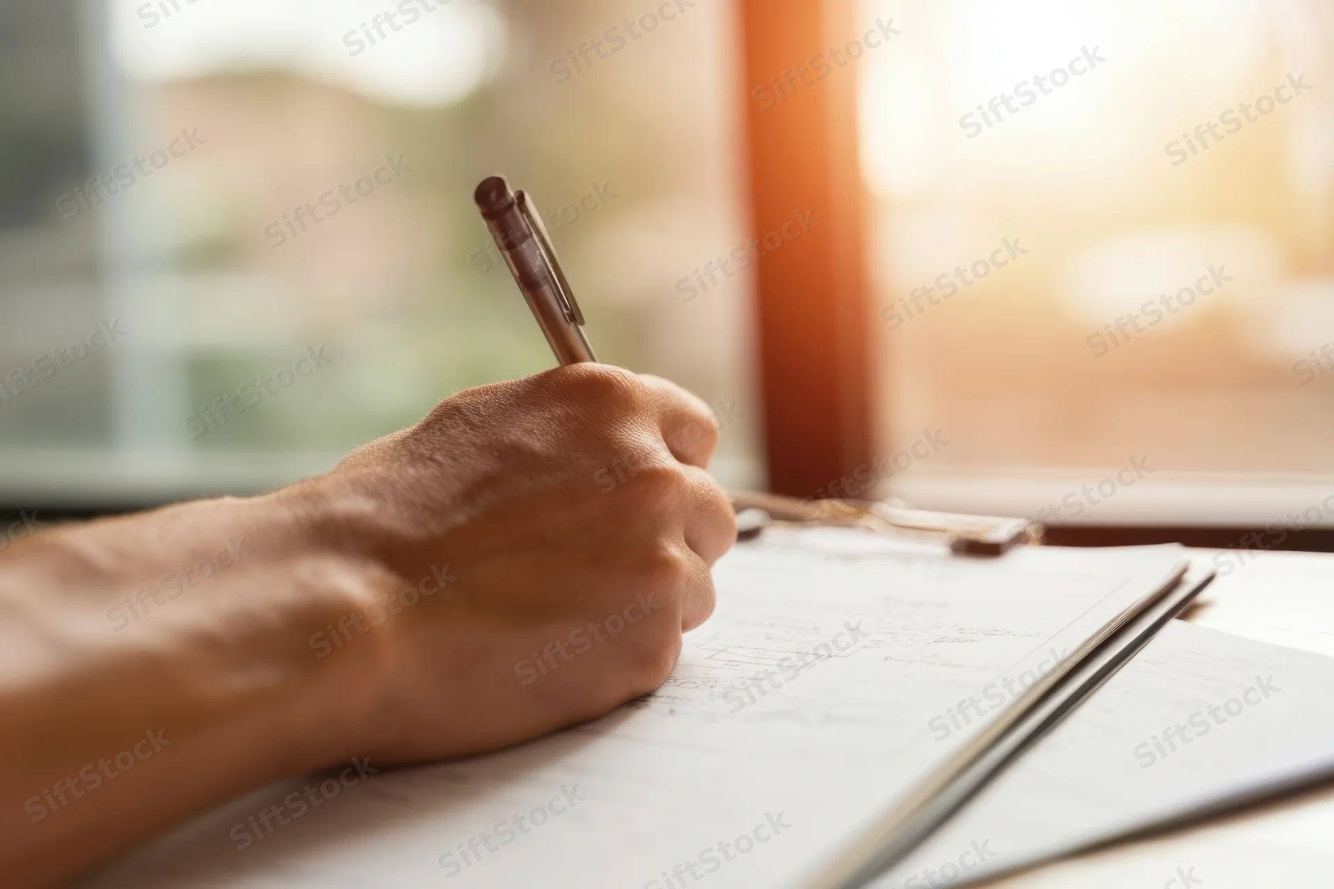 Hand writing with pen on clipboard document near window in office