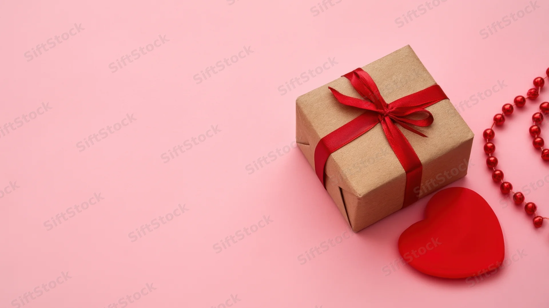 Gift box wrapped in kraft paper with red ribbon and heart on pink background