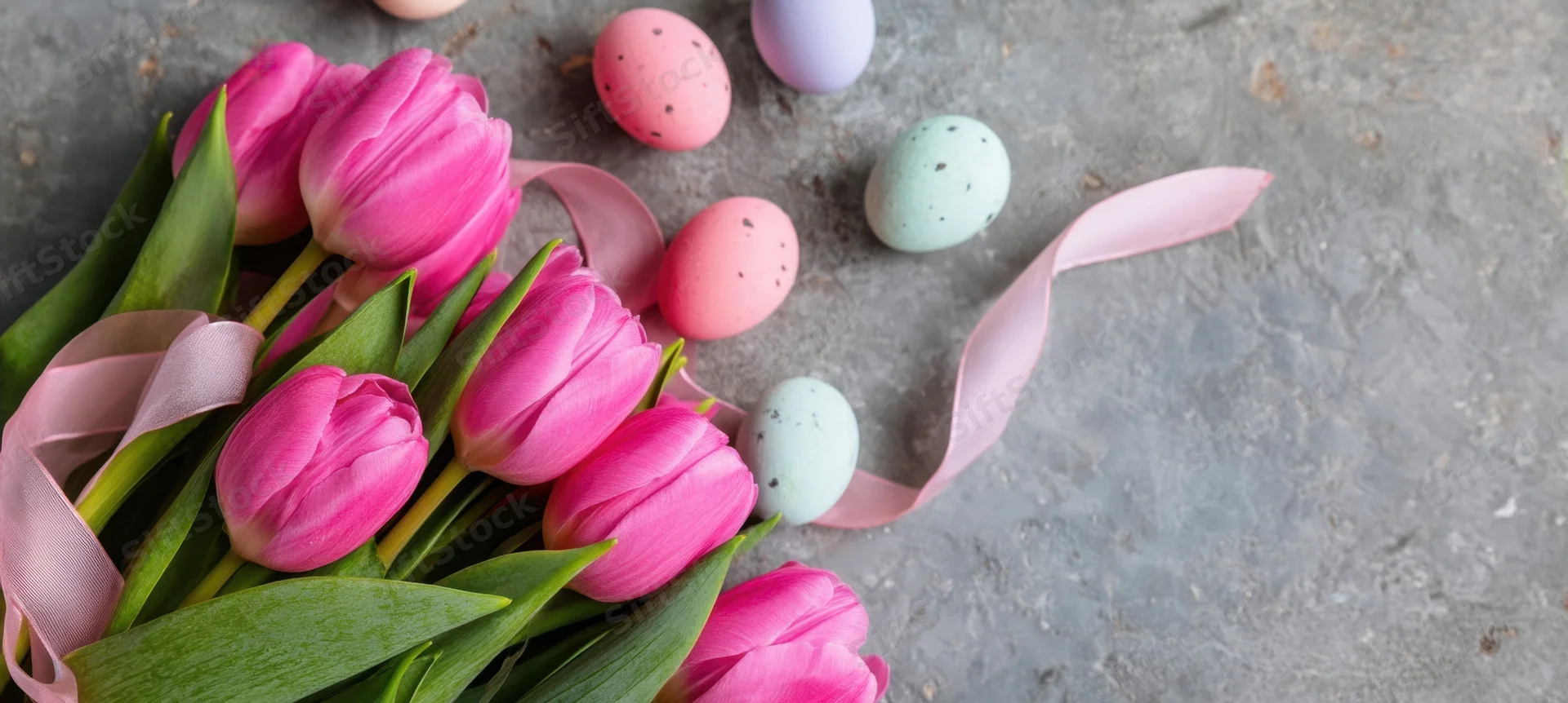 Pink tulips and pastel speckled eggs arranged with ribbon on concrete surface
