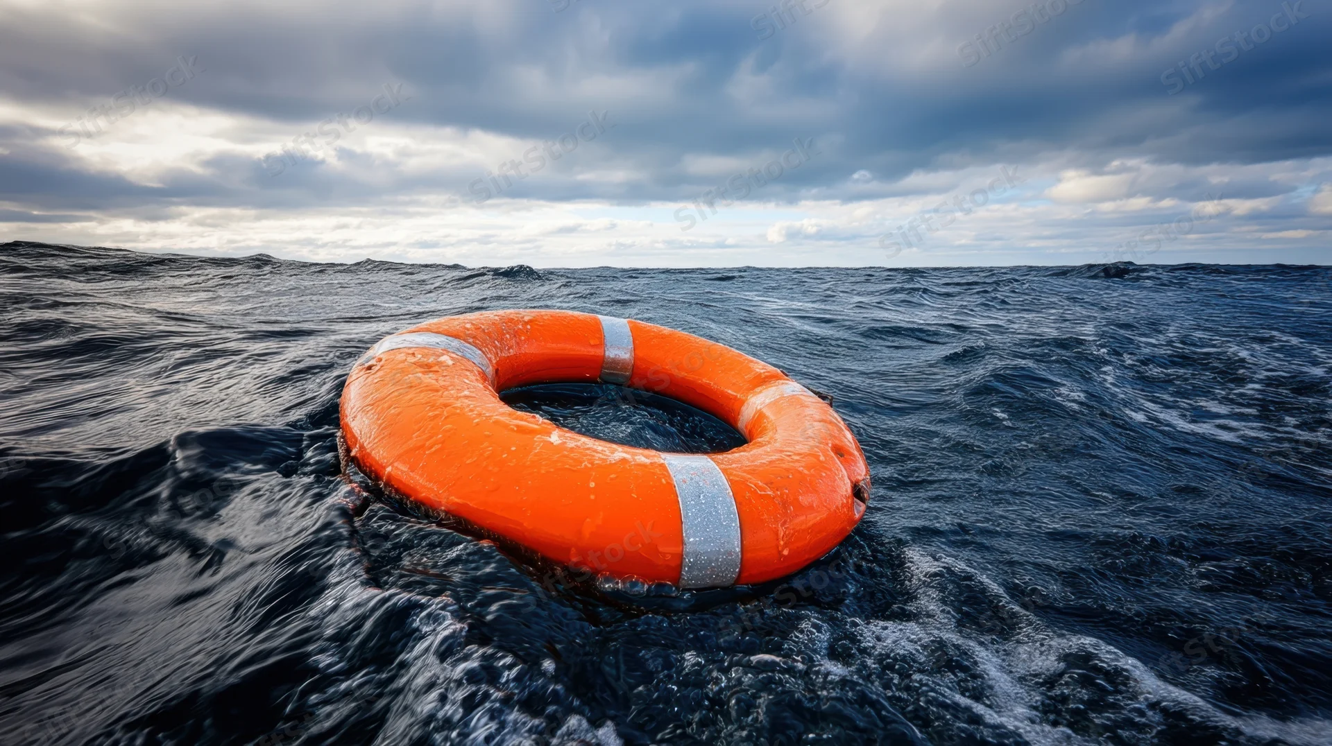 Orange lifebuoy floating on dark ocean waves under cloudy sky
