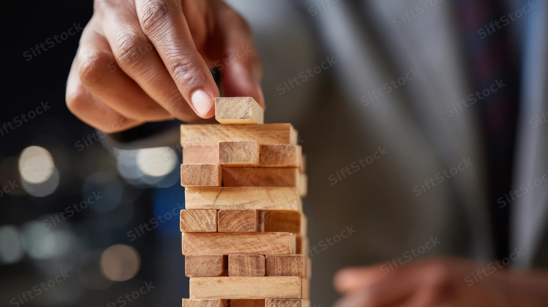 Hand placing wooden block on top of a jenga tower in an office setting at night