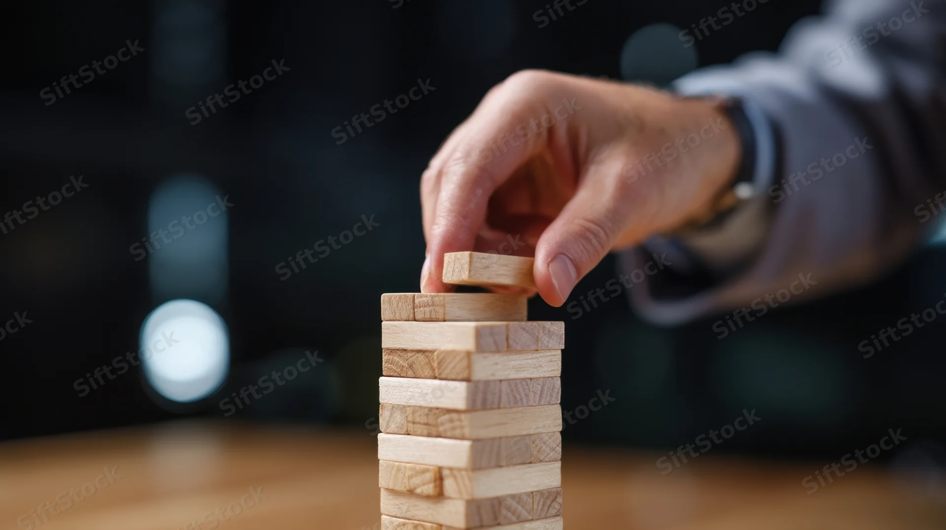 Hand placing wooden block on top of a stack on a table in an office setting