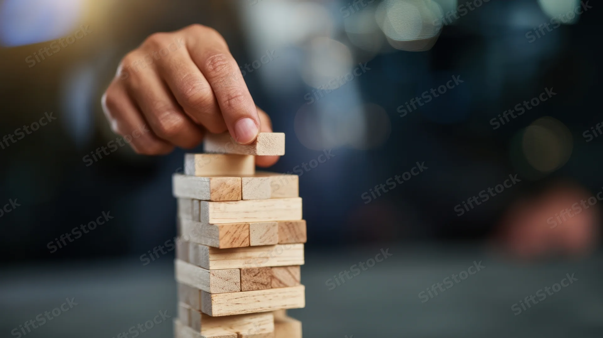 Hand placing wooden block atop a tower of blocks on a table